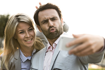Playful business couple taking selfie outdoors on sunny day