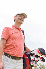 Happy middle-aged man looking away while carrying golf bag against clear sky