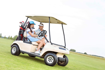 Couple looking at each other while sitting in golf cart against clear sky