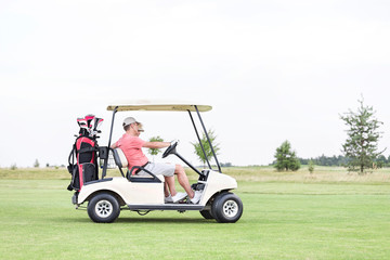 Side view of couple sitting in golf cart against clear sky