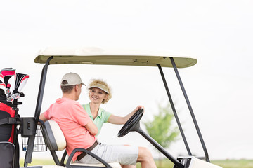 Fototapeta na wymiar Happy woman looking at man while sitting in golf cart