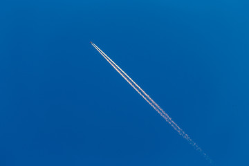 Jet plane leaves double contrail in a shine clear blue sky flying on diagonal