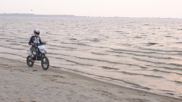 The motorcyclist riding a sport bike on a sand beside the lake at sunset.