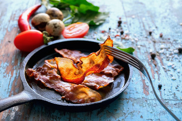 Fried bacon in a pan tomatoes, spinach, hot peppers, aged wooden background