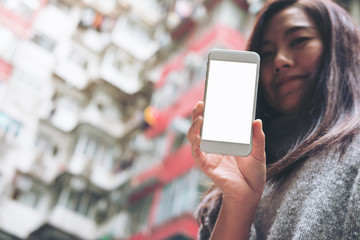 Mockup image of hands holding and showing white mobile phone with blank white screen with a crowded residential building in community in Quarry Bay, Hong Kong background 