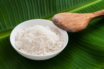 Plain Jasmine rice in white bowl with wooden spoon on banana leaf