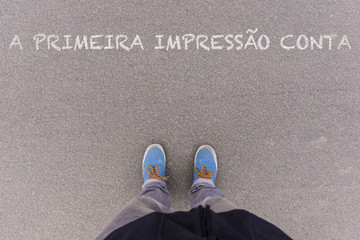 A primeira impressao conta, Portuguese text for First Impressions Count text on asphalt ground, feet and shoes on floor