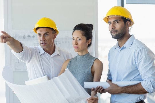 Three Architects Discussing Over Blueprint