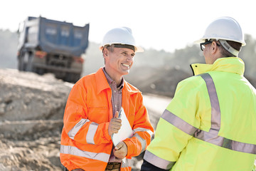 Happy engineer discussing with colleague at construction site on sunny day