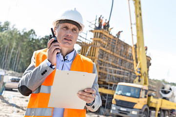 Supervisor using walkie-talkie while holding clipboard at construction site