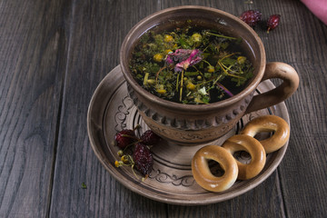 Herbal tea, herbs and flowers in a  clay cup with cookie on wooden table