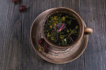 Herbal tea, herbs and flowers in a  clay cup with cookie on wooden table