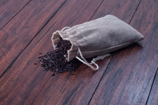 Small sack bag with heap of black rice on wooden desk