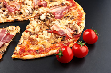Meat pizza with slice and tomatoes isolated on black background