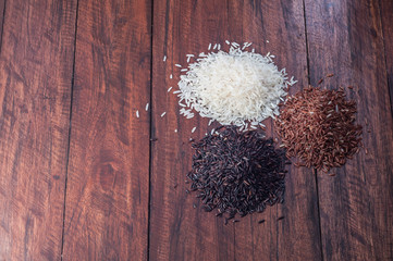 Few heap of different rice on wooden desk. Jasmine white, black and brown rice on kitchen table