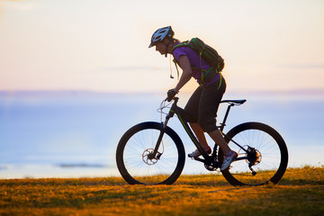 Fototapeta premium Woman mountain biking on single track trail at Sunset