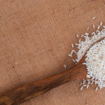 Close up to wooden spoon with heap of White Jsasmine rice on burlap kitchen surface