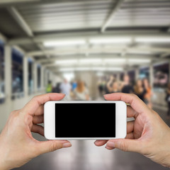 Woman hand holding and using mobile,cell phone,smart phone with isolated screen with blur image of people for background.