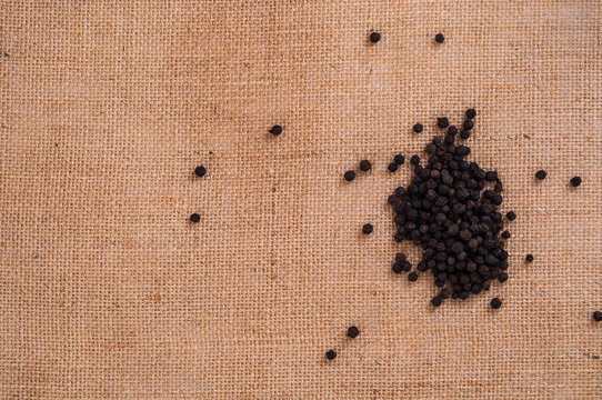 Heap of black pepper on burlap kitchen surface