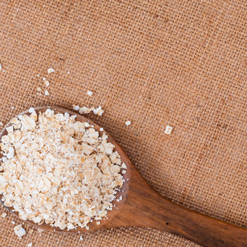 Wooden spoon with Oat flakes meal on burlap surface