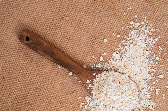 Oat meal on wooden spoon on burlap surface kitchen table