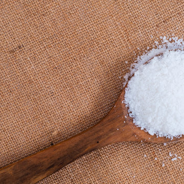 White heap of salt or sugar in wooden spoon on burlap cover surface
