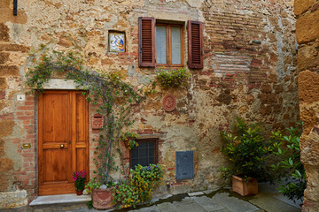 Fototapeta na wymiar Retro wooden door outside old Italian house in a small town of Pienza, Italy. Plants decorations, ivy, vintage