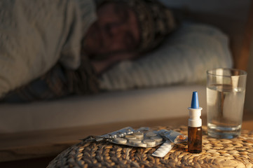 Ein Mann liegt mit Erkaeltung im Bett / Ein Mann liegt mit Erkaeltung im Bett, vor ihm liegen Medikamente, geringe Tiefenschaerfe.