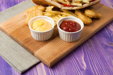 gyros and fries and nuggets on a wooden board with two cups of sauce on the table