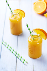 Fresh orange juice in the jar with straw on white wood table. Vertical shot
