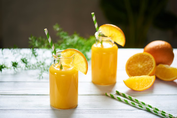 Fresh orange juice in the jar with straw on white wood table. Vertical shot