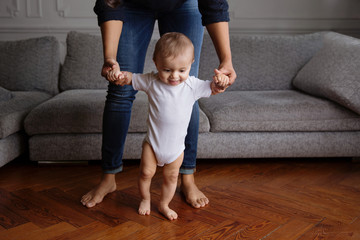 baby learning to walk on a wood floor with his mother holding his hands