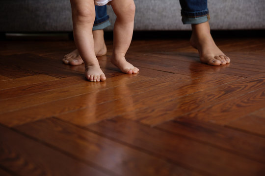 chubby feet of a baby doing his first steps on a wood floor with his mother