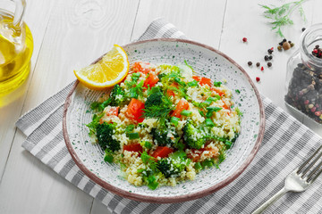 Healthy salad made of couscous, broccoli, tomato, pepper, onion and dill on a white wooden table. Traditional Moroccan food for healthy meal. Top view.