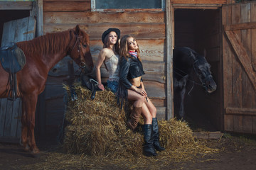 Two women sit on a straw on a farm, the horses stand beside them.