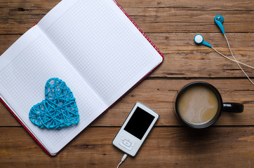 A cup of coffee, a notebook and a player with headphones on a wooden table.