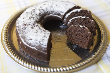Homemade chocolate cake, with sugar glass on top, on a golden tray. Horizontal shot with natural light from a window.