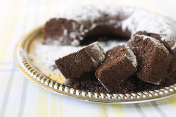 Homemade chocolate cake, with sugar glass on top, on a golden tray. Horizontal shot with natural light from a window.