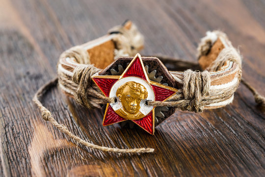 Closeup retro handmade bracelet made of leather and hemp with ussr octobrist symbol - star badge at wooden table.