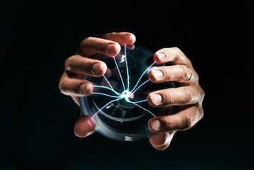 Hands holding a glass ball with electricity, magic.