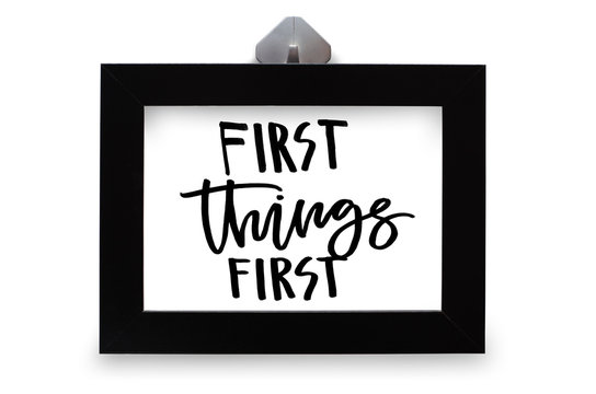 First things first. Handwritten text. Modern calligraphy. Inspirational quote in black wooden frame