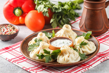 Khinkali - Georgian dumplings with meat and parsley in a ceramic dish with a sauce of sour cream and greens. Selective focus