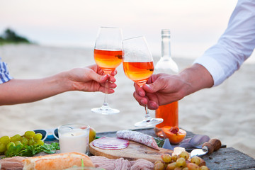 Man and woman clanging wine glasses with rose wine at sunset beach