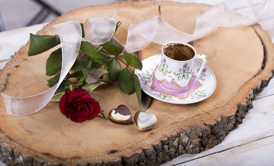Turkish coffee with red rose, heart shaped chocolates and gold rings on wooden  