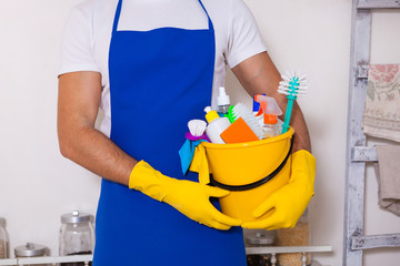 Man holding plastic bucket with bottles and brushes, gloves and detergents in the kitchen