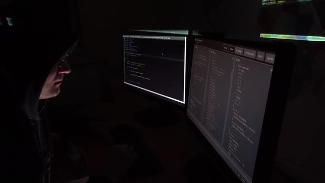 IT programmer in glasses working at the computers in dark room