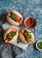 Grilled hot dogs with tomato sauce and chimichurri on wooden background, top view