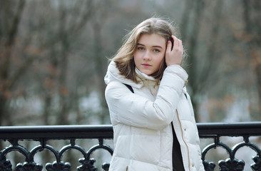 Beautiful young blonde woman standing on the spring city park in warm clothes. Cold season lifestyle freshness concept