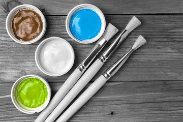 Brush and colorful paint in jars on an old wooden background with copy space in black and white tones