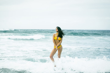 Pretty girl in sexi yellow swimsuit standing on rock